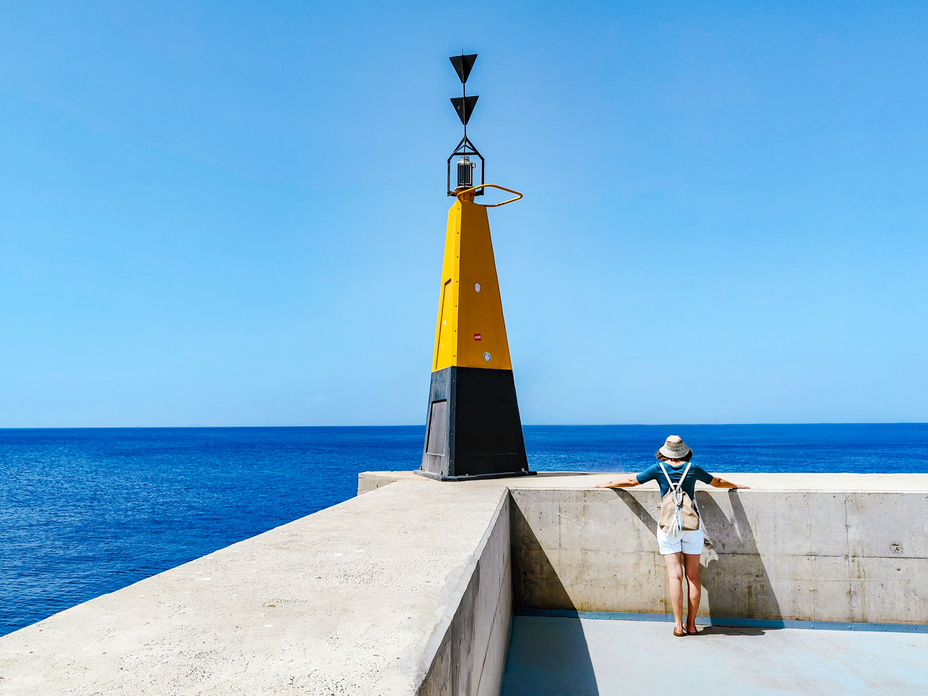 Gelber Leuchtturm und Reisende vor blauem Meer