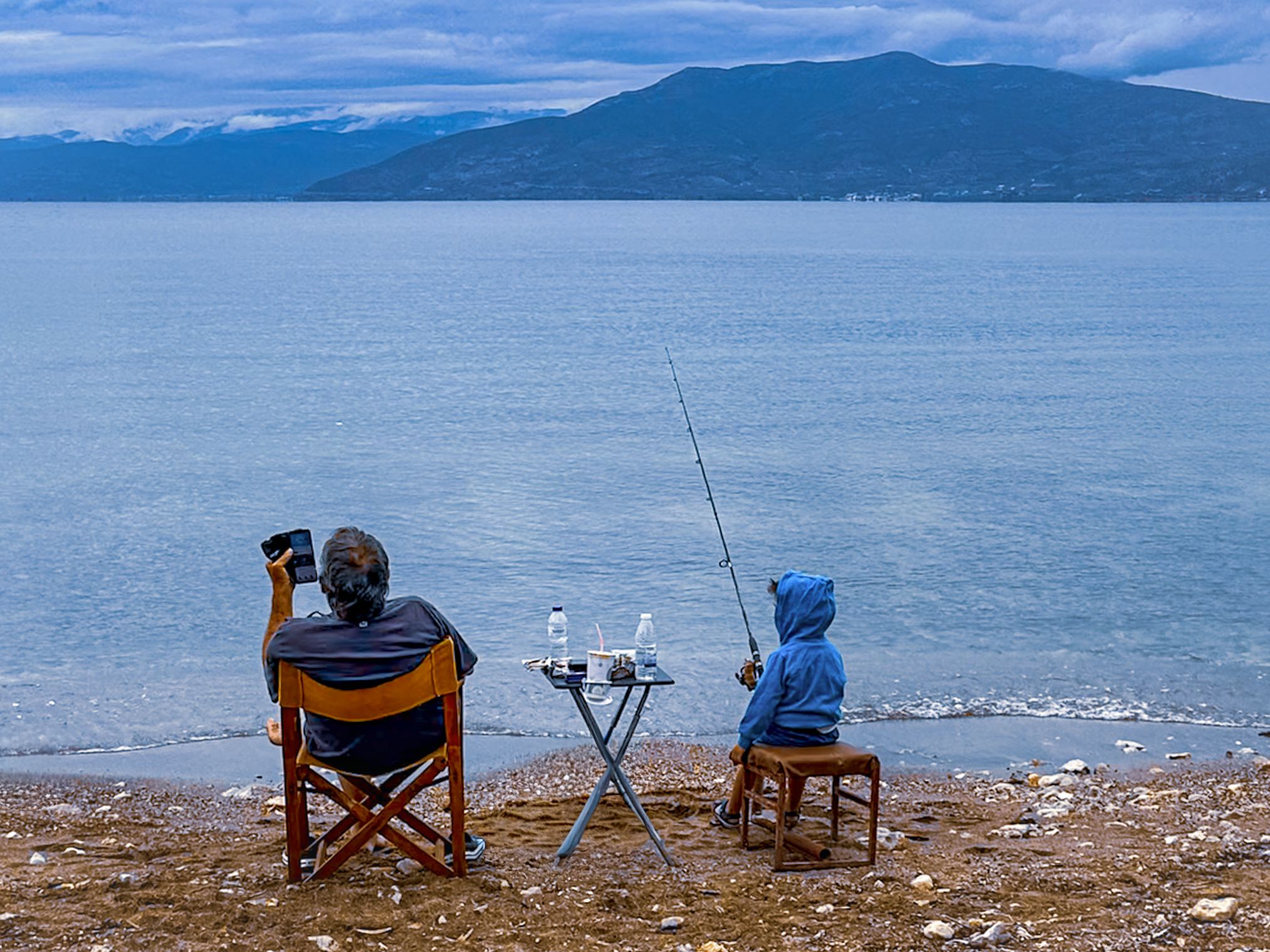 Zwei Menschen sitzen mit Abstand am ruhigen Meer
