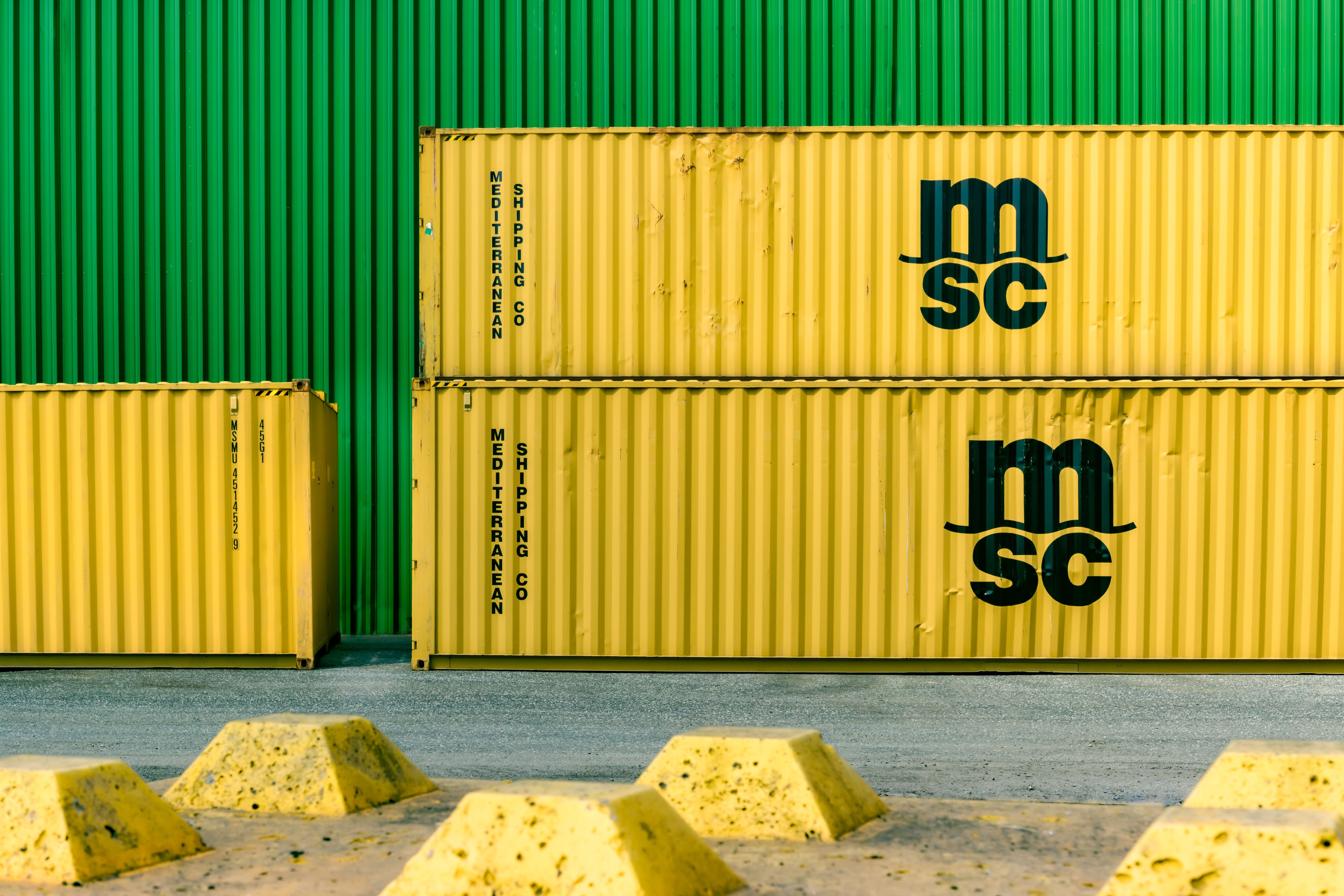 Gelbe Frachtcontainer vor einer grünen Wand